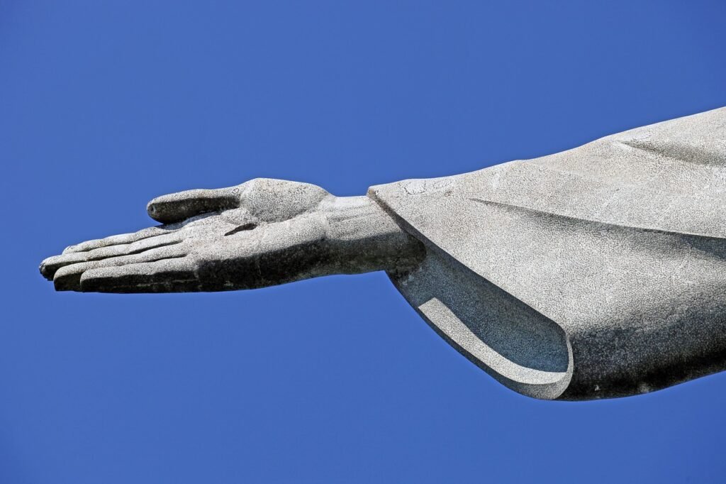 História do Cristo Redentor: Uma Jornada de Fé e Engenharia 1 Braço direito do Cristo Redentor, a foto mostra apenas a mão furada do Cristo e parte da manga da roupa. Céu azul claro.