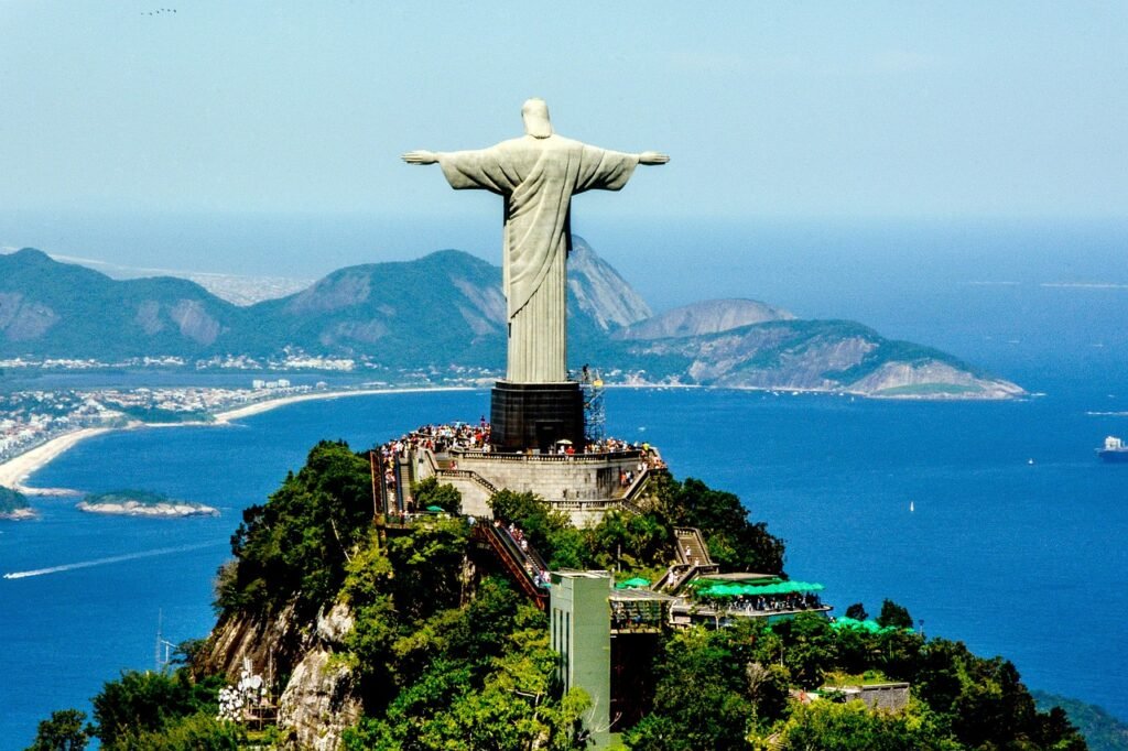 Como chegar ao Cristo Redentor no Rio de Janeiro? 7 Cristo Redentor Visto em dia de sol, mar azul, pessaoas visitando a estátua.