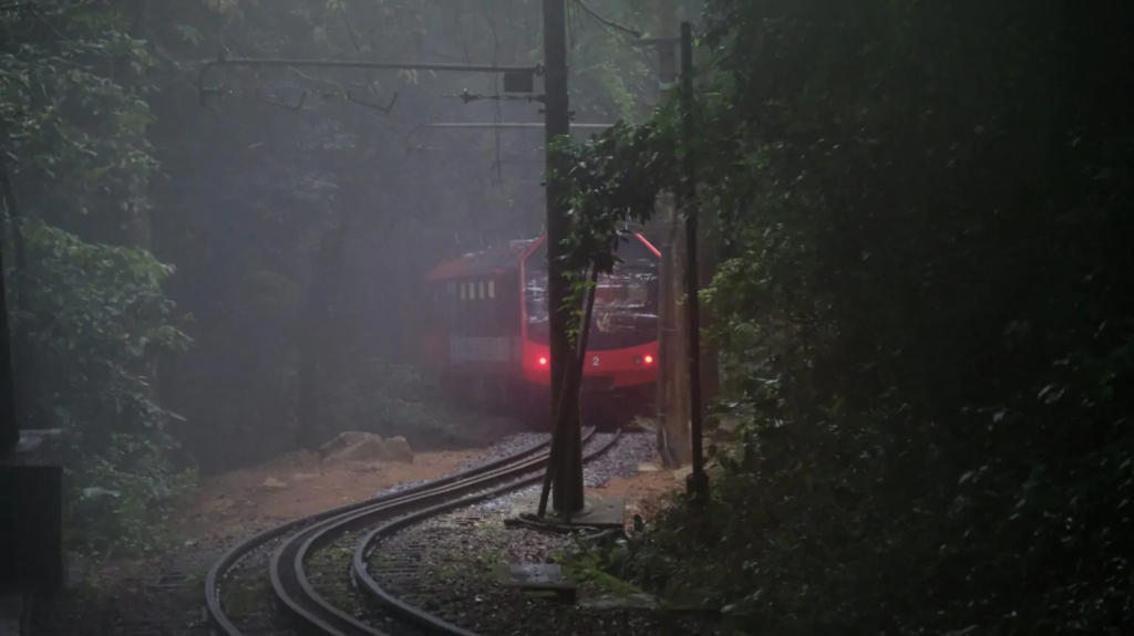 Como chegar ao Cristo Redentor no Rio de Janeiro? 2 Trem do Corcovado saindo de trás das árvores, a floresta da Tijuca está umida e escura. farois do trem acesos.
