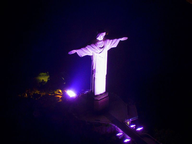 Cristo Redentor: como chegar, ingressos e horários 4 Foto noturna do Cristo Redentor Iluminado em tom lilás.