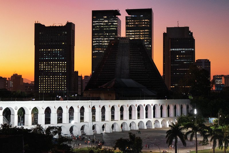 Roteiro Completo: 3 Dias Inesquecíveis no Rio de Janeiro 4 Fotos dos Arcos da Lapa, Rio de Janeiro mostrando a cidade ao fundo iluminada por um belo por do sol.