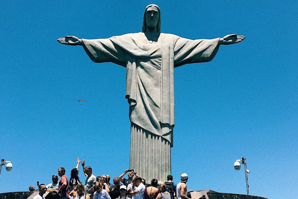 A Estátua do Cristo Redentor: Por que é um dos destinos mais procurados do mundo? 4 Pessoas tirando foto aos pés do Cristo no Rio de Janeiro