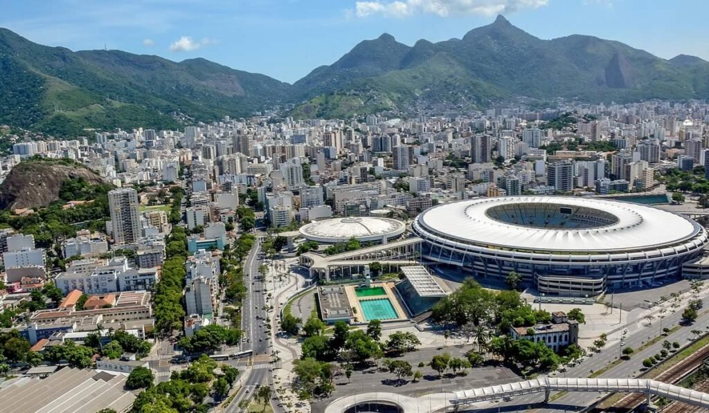 O que fazer no Rio de Janeiro? 10 pontos turísticos 3 Estádio do Maracanã, foto em dia de sol. Ao fundo a cidade do Rio de Janeiro e as montanhas.